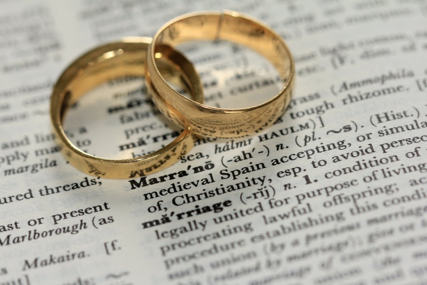 Two gold wedding rings sit on a page from a dictionary, near the definition of marriage.