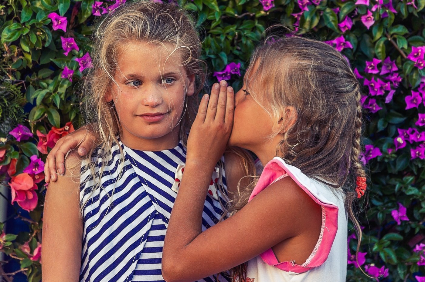 A girl whispers her secret into the ear of a nearby friend.